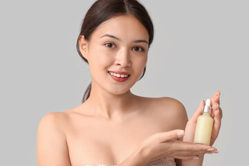 Sticker - Beautiful young Asian woman with bottle of cosmetic oil on grey background