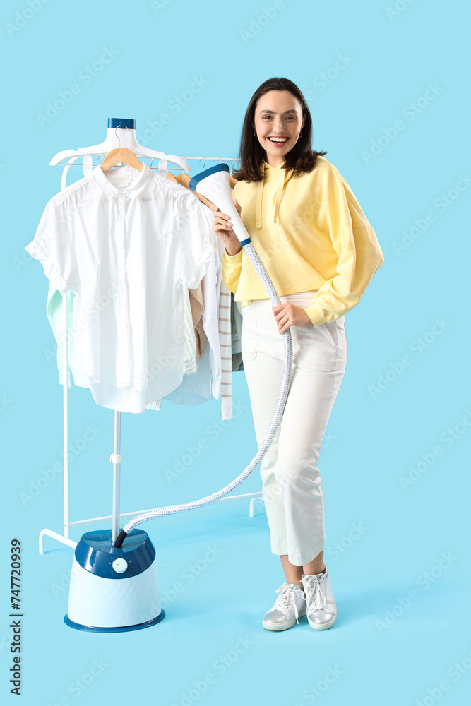 Pretty young woman with modern steamer and clothes on blue background
