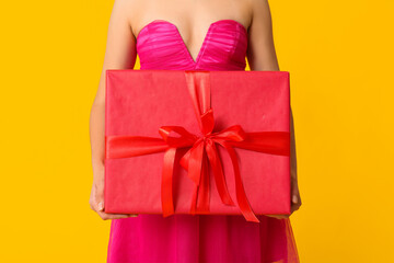 Poster - Beautiful young woman with gift box on yellow background. Valentine's Day celebration