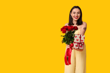 Wall Mural - Beautiful young happy woman with gift box and bouquet of roses on yellow background. Valentine's Day celebration