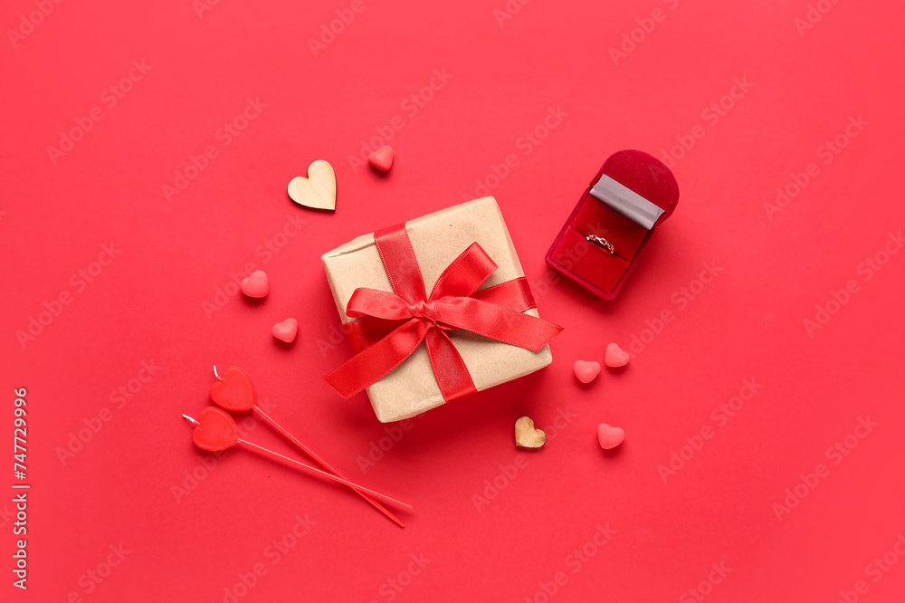 Composition with engagement ring, gift box and decor for Valentine's Day celebration on red background
