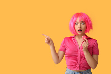 Poster - Beautiful young woman in pink wig with sweet macaroon pointing at something on yellow background