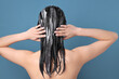 Asian woman applying hair mask on blue background, back view