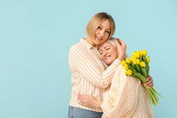 Poster - Adult woman with bouquet of tulips hugging her mother on blue background. International Women's Day celebration