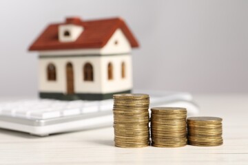 Wall Mural - Mortgage concept. Stacks of coins, model house and calculator on white wooden table, selective focus