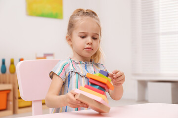 Sticker - Cute child playing with colorful wooden stacker at table in room