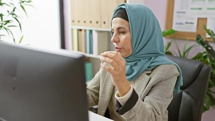 Sticker - A mature muslim woman in a hijab working in an office, adjusting glasses and feeling stressed in front of a computer.