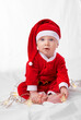 © T. Rose/peopleimages.com - Baby, portrait and cute with santa costume for first Christmas holiday, star lights and white background. Boy toddler, xmas and outfit for festive season or celebration, innocent and adorable in hat.