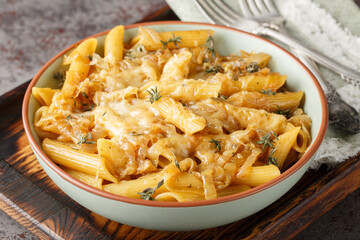 Wall Mural - Delicious French onion pasta penne with caramelized onions, fragrant thyme, garlic and gruyere cheese close-up on a bowl on a wooden board. Horizontal