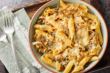 Wall Mural - French Onion Pasta features plenty of caramelized sweet onions, fresh thyme, al dente penne and cheese closeup on the bowl on the wooden board. Horizontal top view from above