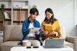 © Nuttapong punna - Two Attractive young Asian female college students working on the school project using laptop computer and tablet together, enjoy talking and snacking on sofa