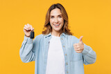 Fototapeta Panele - Young smiling happy woman she wear blue shirt white t-shirt casual clothes hold in hand car keys fob keyless system show thumb up isolated on plain yellow background studio portrait Lifestyle concept