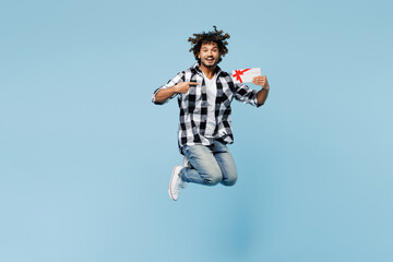 Wall Mural - Full body young Indian man wears shirt white t-shirt casual clothes jump high hold point finger on gift certificate coupon voucher card for store isolated on plain blue background. Lifestyle concept.