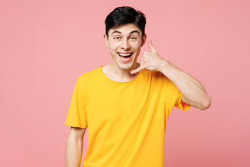 Wall Mural - Young surprised happy Caucasian man he wears yellow t-shirt casual clothes doing phone gesture like says call me back isolated on plain pastel light pink background studio portrait. Lifestyle concept.