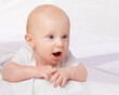 © T. Rose/peopleimages.com - Cute baby, child and shocked on bed for curiosity, reaction and surprise with laying in nursery at house. Adorable, kid and excited infant in home to relax, observe or wonder for development