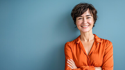 Confident mature woman smiling in orange blouse against a blue background, exuding positivity.