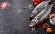 Fresh raw seabass with spices and tomatoes on a branch. On black rustic background