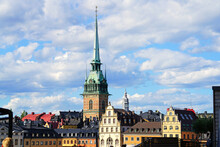 Traditional Buildings With Roofs And Colorful Walls And Spires Of Lutheran German Church On Kornhamnstorg Harbour Square In Old Historical Town Quarter Gamla Stan, Stockholm, Sweden
