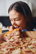 Woman eating pizza with open mouth and drink in front of her in a casual setting
