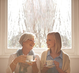 Canvas Print - Family, happy woman and senior mother drinking coffee at breakfast, talking and smile. Laughing, elderly mom and daughter with tea cup, conversation and listening to funny story at home together