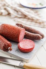 Poster - Sliced smoked salami sausages on cutting board on white table.