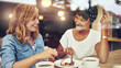 © Flamingo Images - Two young smiling multi ethnic women sit in the window of a cafe. They drink coffee and share a dessert