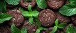 A heap of decadent chocolate peppermint cookies topped with vibrant green leaves, creating a visually appealing contrast in colors and textures. The cookies are arranged in a haphazard yet inviting