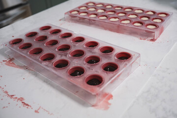 Two plastic chocolate molds filled with pink chocolate. Chocolate filled filling inside.