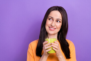 Wall Mural - Photo of toothy beaming woman dressed orange t-shirt hold mug of coffee look empty space offer isolated on purple color background