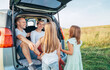 © Soloviova Liudmyla - Portrait of Happy young couple with little daughters sitting inside car trunk during auto trop. They are smiling, laughing and chatting. Family values, traveling concept.