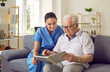 © Studio Romantic - Happy elderly man together with a friendly nurse sitting on the sofa in the retirement home, reading an interesting book and enjoying quiet pastime. Senior care concept