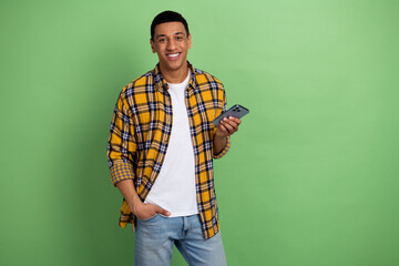 Photo of young smiling man in checkered shirt student using smartphone searching wifi at university isolated on green color background