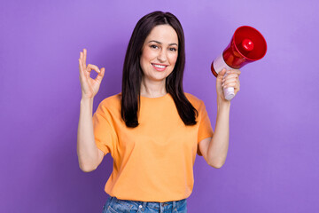 Canvas Print - Portrait of mature age business woman in yellow t shirt okey gesture using loudspeaker at demonstration isolated on purple color background