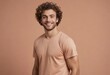 © kotlyarn - A cheerful man with curly hair smiles in a peach t-shirt. His casual pose and joyful expression convey a friendly and lively spirit.