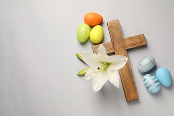 Wall Mural - Wooden cross, painted Easter eggs and lily flowers on grey background, flat lay. Space for text