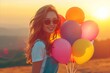 Happy young woman with colorful balloons at sunset. Freedom and happiness concept.