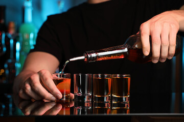 Canvas Print - Bartender pouring alcohol drink into shot glass at mirror counter in bar, closeup