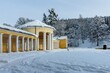 Marienbad, Czech Republic - December 4 2023: Yellow and white building of Ferdinand Spring pavilion during winter time covered with snow. Sunny evening in the park.