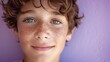 Joyful boy with curly hair and freckles smiling. Expressive blue eyes of a cheerful young boy. Portrait of happiness in a child with a purple backdrop.