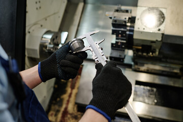 High angle view closeup of hands of unrecognizable turner measuring size of metal part