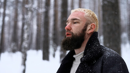 Wall Mural - Man relaxing in the winter forest, the concept of unity with nature. Media. Young blond man thinking about life in snowy wood.