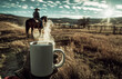 a steaming cup of coffee on the open range with cowboys riding in the distance