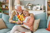 Fototapeta  - Anniversary surprise - Senior man presents flowers to his wife at home