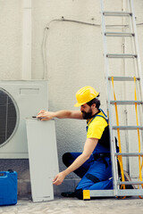 Wall Mural - Experienced serviceman starting work on broken air conditioner, using pneumatic drill to pull apart condenser metal coil panel. Certified electrician taking apart hvac system to check for leaks