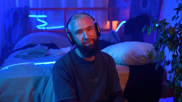 Music lover, young man in headphones, neon light portrait. Media. Relaxed guy in wireless headphones putting them off.