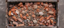 A Close-up View Of A Metal Waste Container Filled With Red Brick Debris, Likely From A Demolished Building. The Bricks Are Loosely Stacked Inside The Container, Creating A Messy And Industrial Scene.