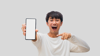 Young Asian man wearing a white t-shirt making a wow face showing mobile phone with blank white smartphone screen isolated on gray background. Guy recommending new application or mobile website