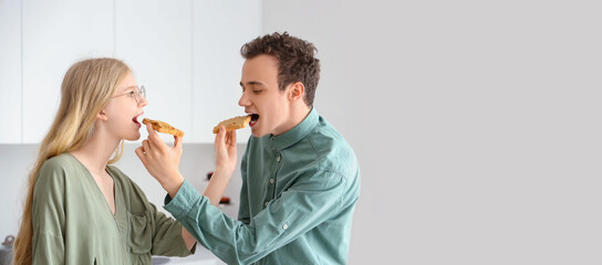 Young beautiful couple feeding each other tasty toasts of nut butter in kitchen