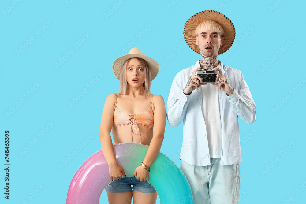 Shocked young couple with inflatable ring and photo camera on blue background