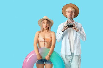 Wall Mural - Shocked young couple with inflatable ring and photo camera on blue background